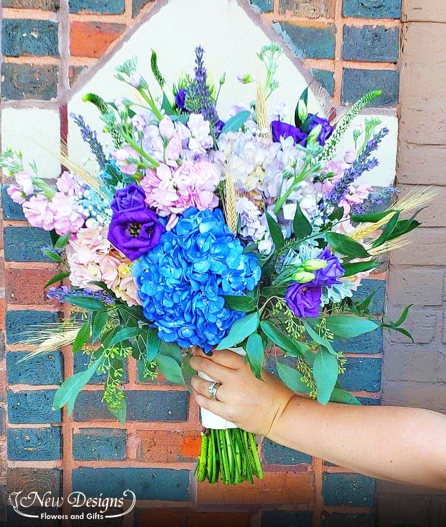 A stunning bouquet of ombre Pink Purple and Blue Hydrangeas and Stock, with wheat stems spiking through
